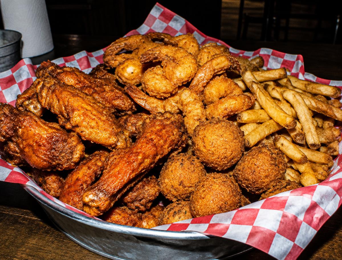 Crispy wings, fried shrimp, hush puppies, and fries in a metal basket
